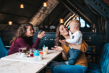 Two friends enjoying in cafe bar with cute little baby boy.
