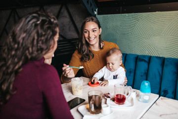 Two friends enjoying in cafe bar with cute little baby boy.