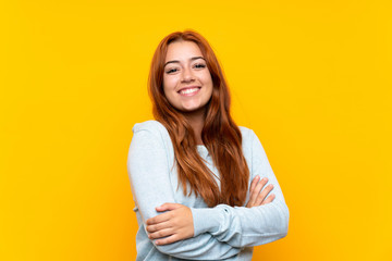 Teenager redhead girl over isolated yellow background keeping the arms crossed in frontal position