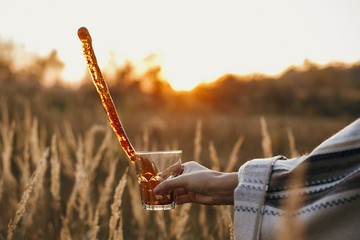 Hand spilling hot coffee from glass cup in sunny warm light on background of countryside rural...
