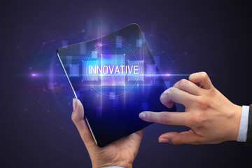 Businessman holding a foldable smartphone with INNOVATIVE inscription, new technology concept