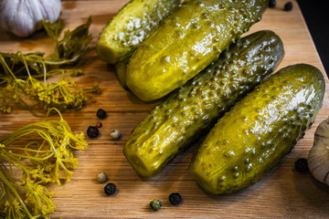 Pickles lie on a wooden board, next - garlic, dill and peppercorns. Dark background. The concept of fermented food.