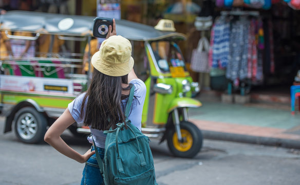 Traveller woman holding camera on the trip in Thailand with traditional TUK TUK car in background. 