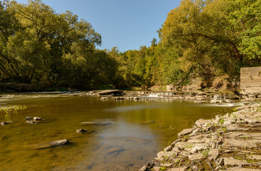 old broken weir on a river under trees in summer