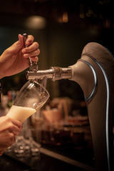 Close up chrome tap bartender holding a glass during pouring cold draft beer from dispenser, selective focus, background copy space, night time