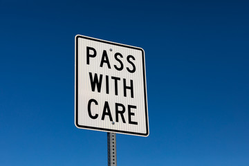 closeup angled view of pass with care reflective street sign. Isolated on deep blue sky background