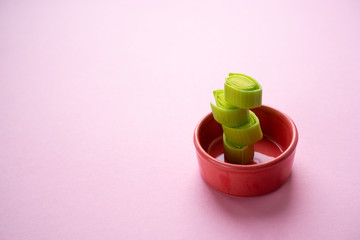 Chopped leek and stacked in a ceramic bowl on a light pink smooth cardboard surface