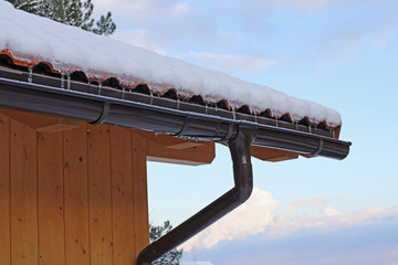 Dachrinne mit Schnee und Eiszapfen an einem Holzhaus mit Regenrinne im Winter