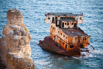 Sunken rusty cargo ship in still blue sea waters with rocks around on summer clear day. Still...