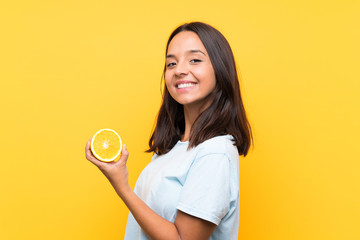 Young brunette woman holding an orange smiling a lot