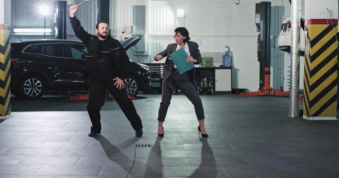 Best team at auto service center office worker woman and mechanic man dancing in the middle of garage funny and excited