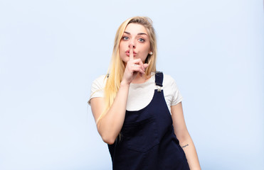 young pretty blonde woman looking serious and cross with finger pressed to lips demanding silence...