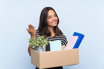 Young brunette girl making a move while picking up a box full of things inviting to come with hand....