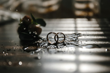 Beautiful toned picture with wedding rings lie on a wooden surface against the background of a bouquet of flowers