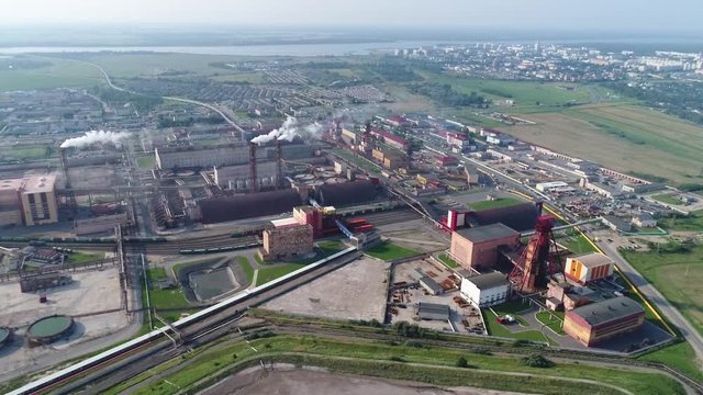 Flying over the potash industry, large pipes emit puffs of smoke, the sky covered with smoke, in warehouses and buildings, left flight