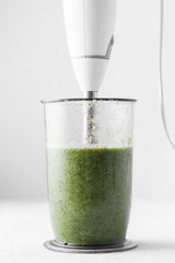 Cooking green smoothie in a blender on a light background. Close up. Fresh green smoothie in a blender. Top view. Freshly prepared vegetarian smoothies from shpenata cabbage and kale.