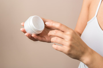 closeup view of woman hands holding a white jar and applying cream