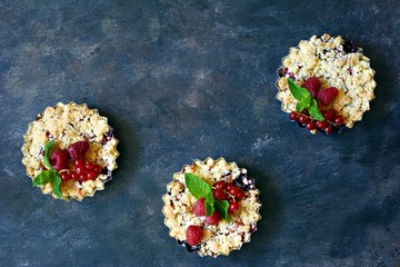 Portion berry crumble crisp in a baking dish on a dark background. Berry tartlets with shortcrust...