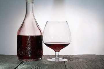 A glass of dry red wine. Bottle of wine. Stand on wooden boards. Shot in backlight.