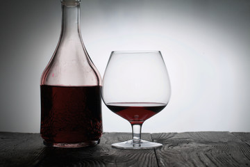 A glass of dry red wine. Bottle of wine. Stand on wooden boards. Shot in backlight.