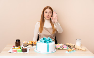 Obraz na płótnie Canvas Young redhead woman with a big cake making stop gesture with her hand