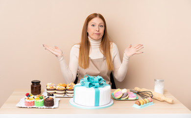 Obraz na płótnie Canvas Young redhead woman with a big cake having doubts with confuse face expression