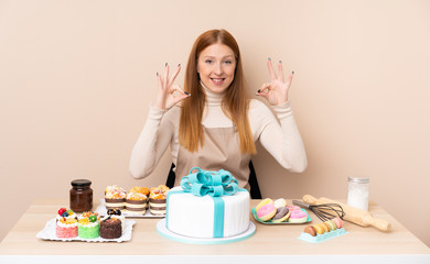 Obraz na płótnie Canvas Young redhead woman with a big cake showing an ok sign with fingers