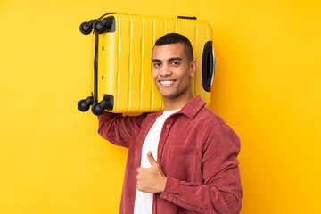 Young African American man over isolated yellow background in vacation with travel suitcase and with thumb up