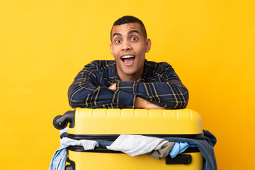 Traveler man with a suitcase full of clothes over isolated yellow background