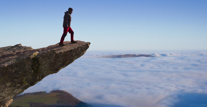 man standing on the cliff above the mountains and clouds - Powered by Adobe