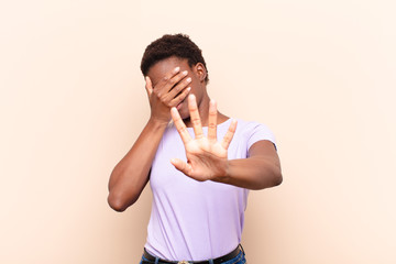 young pretty black womancovering face with hand and putting other hand up front to stop camera,...