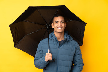 Young handsome man holding an umbrella over isolated yellow background smiling a lot