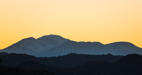 Golden yellow sky at sunset over snow-capped mountains and ridges above Joshua Tree National Park