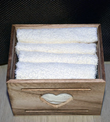 Wooden box for white towels. Face towel. Skin care. White towels in a wooden box on a brown background.
