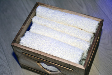 Wooden box for white towels. Face towel. Skin care. White towels in a wooden box on a brown background.