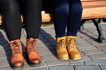 Girls in boots sit on a bench on a Sunny evening. Young girls in half-boots are resting on a bench. Concept: friendship, joint walk of friends.