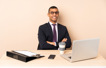 Young business man in his office with a laptop and other documents with arms crossed and looking forward