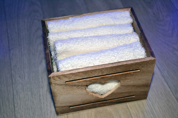 Wooden box for white towels. Face towel. Skin care. White towels in a wooden box on a brown background.