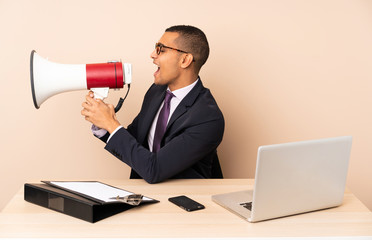 Young business man in his office with a laptop and other documents shouting through a megaphone