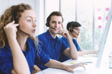 Happy and smiling man of call center worker wear microphone headset during telemarketing job with team. Smiling customer support operator at work.