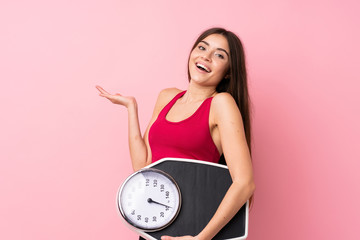 Pretty young girl with weighing machine over isolated pink background with weighing machine - obrazy, fototapety, plakaty