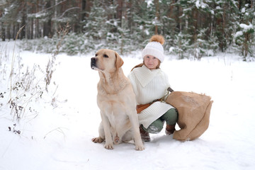 a little girl in white knitted clothes walks in the forest with her dog Labrador. looking for game or tree for home