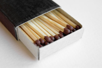 Long wooden safety matchsticks stacked in cardboard matchbox on white background.