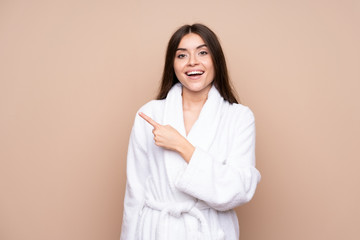 Young girl in a bathrobe over isolated background pointing finger to the side