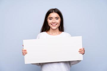 Fototapeta premium Young woman over isolated blue background holding an empty white placard for insert a concept