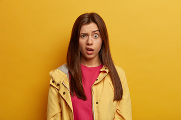 Portrait of disappointed unhappy woman has surprised unhappy reaction, raises eyebrows, smirks face from seeing something unpleasant, wears yellow jacket, poses in vivid studio. Emotions concept © WHstudio Leushin N