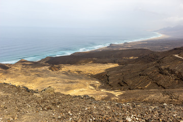 Panoramic view at the coastline in the natural park of Jandia (Parque Natural De Jandina) on canary island Fuerteventura with gravel, lava rocks and rough sea with waves and mountain range