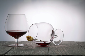 Glasses with red dry wine. One of them lies on its side with the remains of wine. The glass has a dried rose flower. Stand on wooden boards. Shot in backlight.