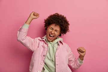 Overjoyed Afro American student makes victory dance, exclaims happily, being on cloud nine,...