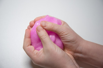 Child's hands close-up. The child kneads the mucus. The mucus is pink and shiny. Slime takes interesting forms.